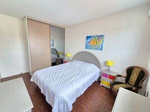 Une chambre à coucher avec un lit, des tables de chevet, une chaise, une armoire et un tableau au mur.