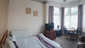 Une chambre d’hôtel équipée d’un lit, d’une télévision, d’un bureau avec des chaises et d’une fenêtre avec des rideaux.