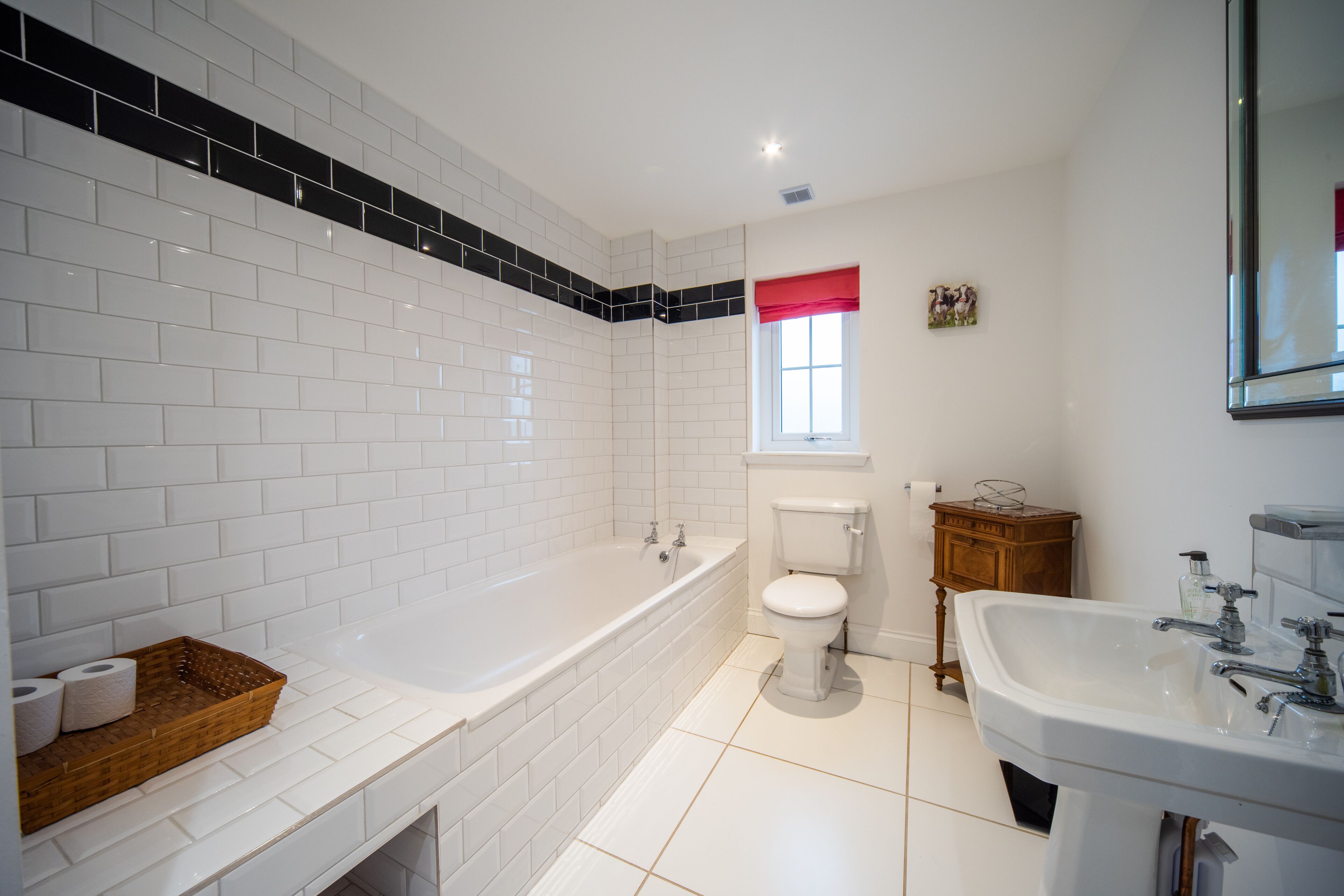 Et moderne badeværelse med hvide fliser, et badekar, et toilet og en vask.