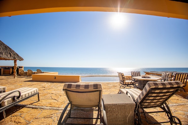 Relax on the beachfront patio with lounge chairs and a dining table, offering a tranquil ocean view.