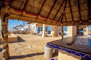 Relax in a serene outdoor space with a thatched roof, stone patio, and comfortable lounge chairs.