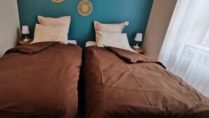 A double bed with brown bedding, two bedside tables with lamps, and a teal wall with a circular decoration. - 4* family apartment, terrace, garden and fireplace (Briançon)