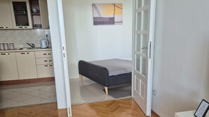 Habitación pequeña con cama, kitchenette y una puerta que da a otra habitación.