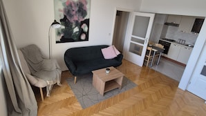 Una sala de estar moderna con un sofá negro, un sillón estampado, una mesa de centro y un cuadro en la pared.