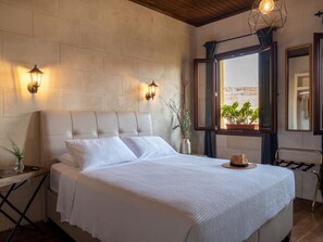 Una cama bien hecha con cabecera, dos lámparas de pared, una ventana con vistas y un espejo en la pared.