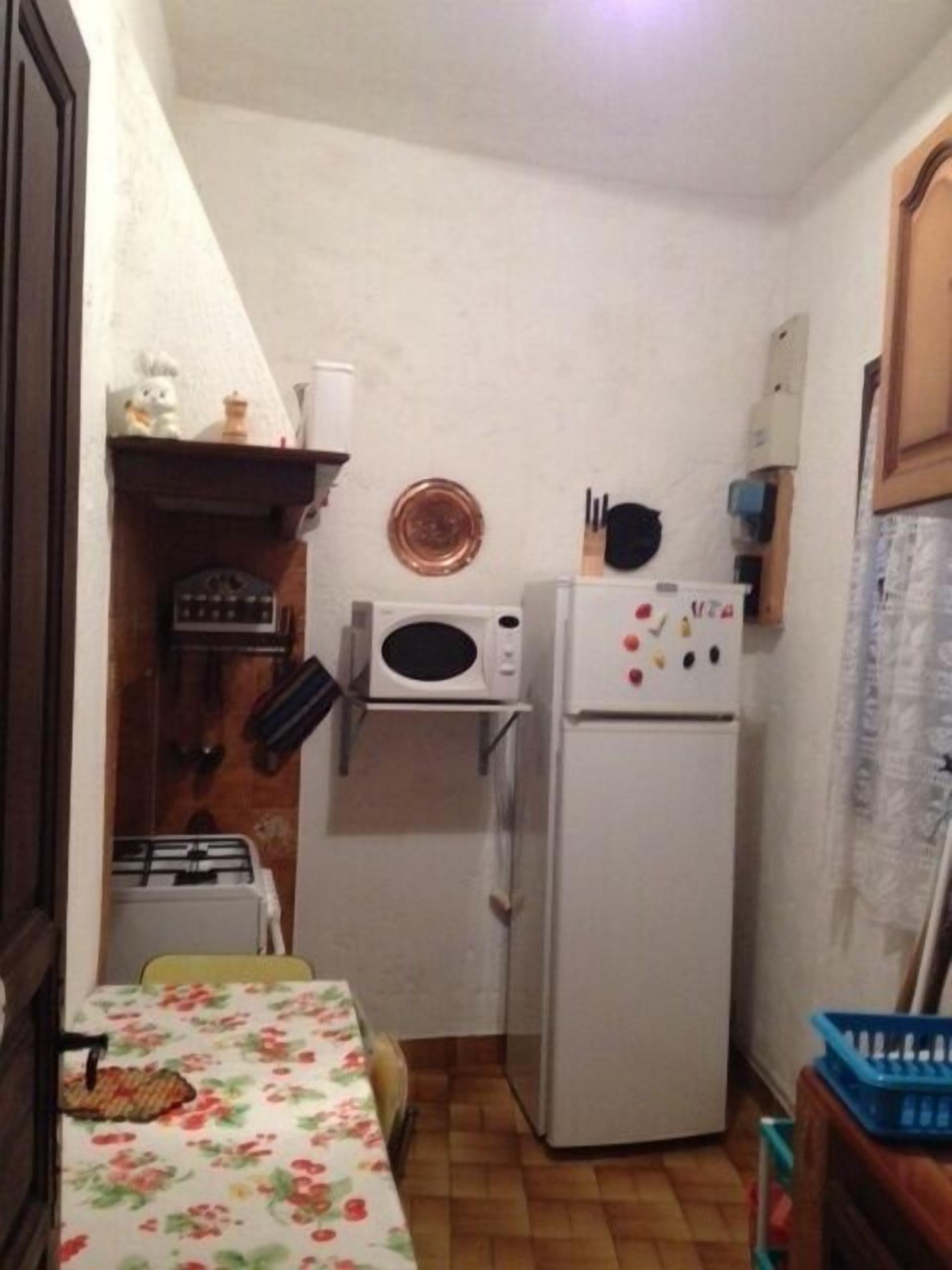 A small kitchen with a microwave, a refrigerator, a sink, and a table with a floral tablecloth.