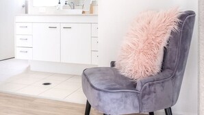 A modern bathroom with a white vanity, a mirror, and a grey chair with a fluffy pillow. - Golden Beach Family Home with Pool (Golden Beach)