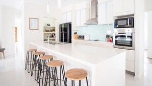 A modern kitchen with white cabinetry, a central island with stools, and built-in appliances including a microwave and oven. - Golden Beach Family Home with Pool (Golden Beach)