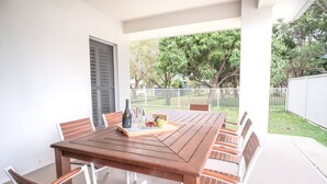 A covered patio with a wooden table and white chairs, a bottle, and a fruit tray. - Golden Beach Family Home with Pool (Golden Beach)