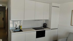 Una cocina compacta con armarios blancos, un lavamanos y una cafetera.