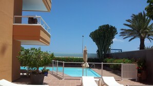 Zona de piscina con sillones, una piscina y vistas al mar.
