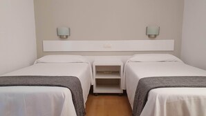 Habitación de hotel con dos camas individuales, un escritorio pequeño y una mesita de noche.