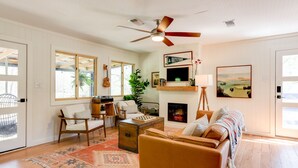 Un salón acogedor con suelo de madera, ventilador de techo, chimenea y un gran ventanal.