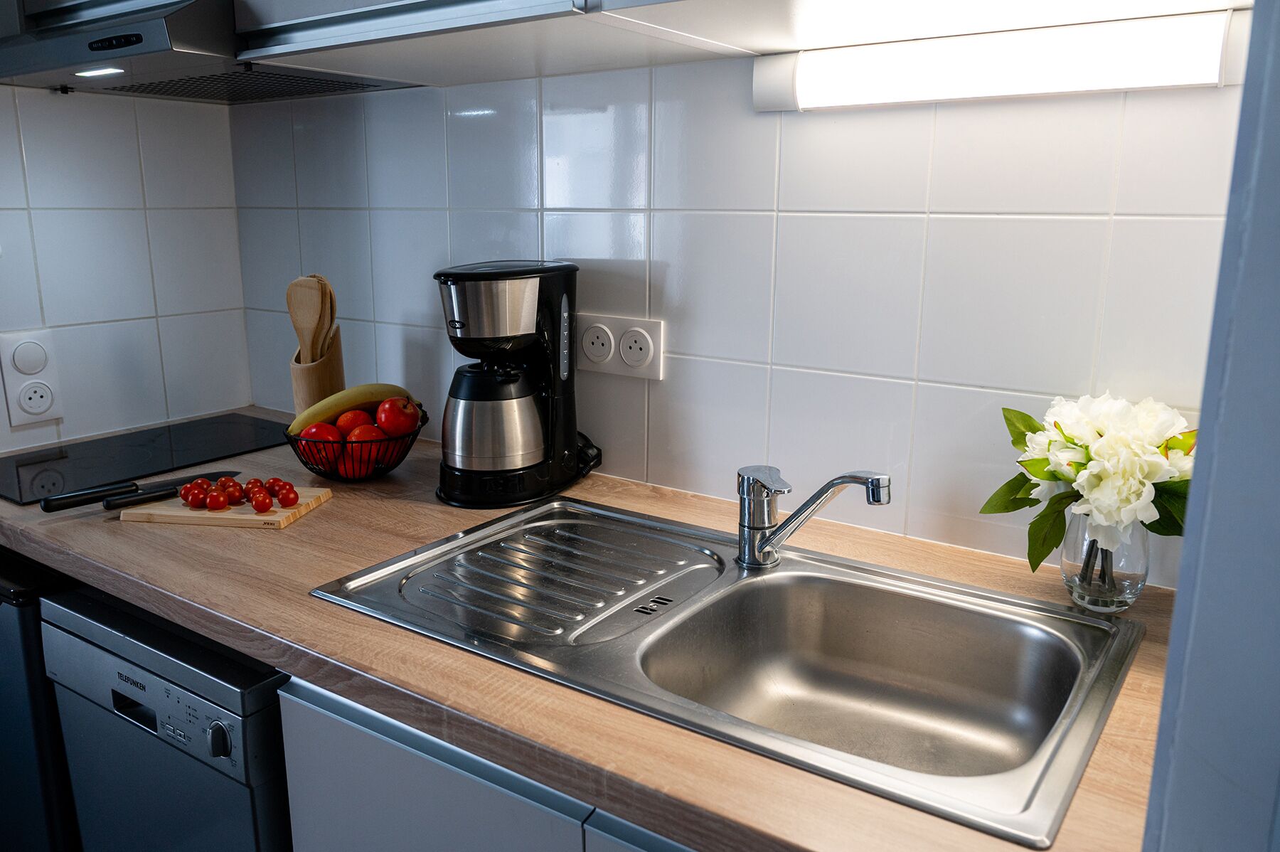 A modern kitchen with a stainless steel sink, a coffee maker, and a fruit bowl on the counter.