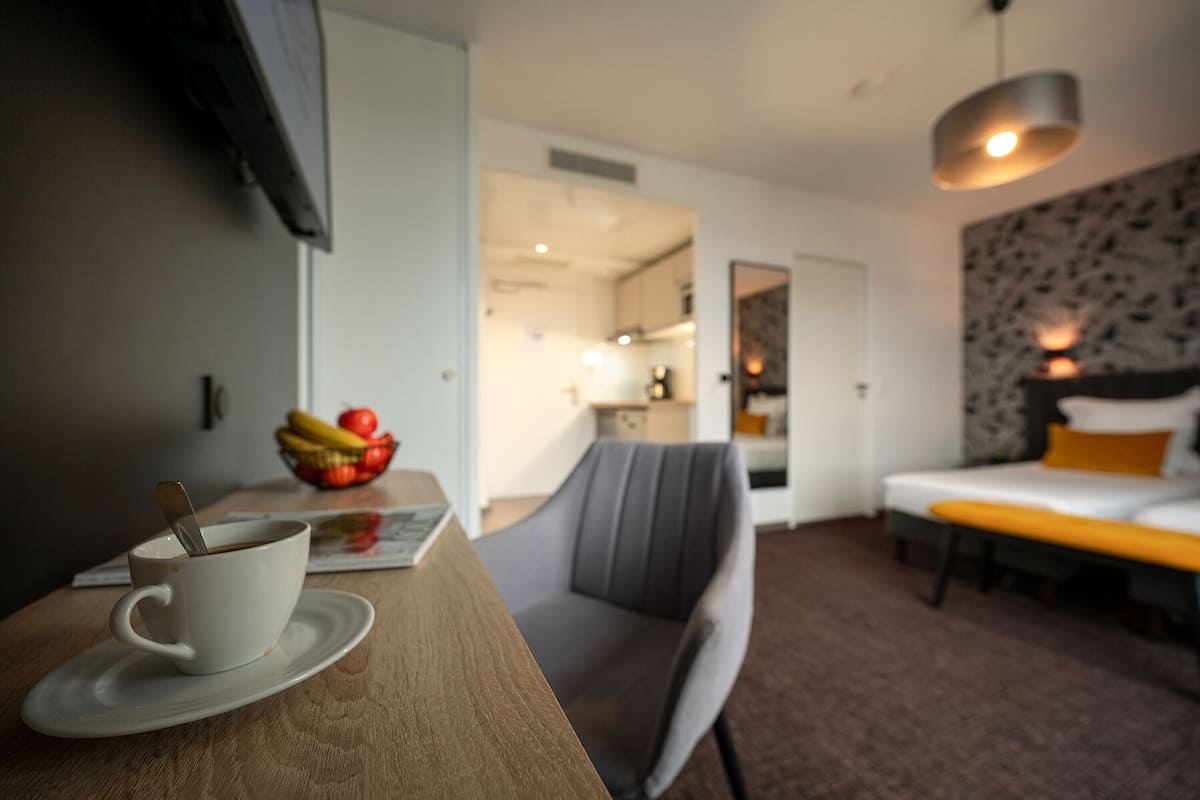 Une chambre d’hôtel avec une table à manger, une tasse de café, un panier de fruits, un lit et un luminaire moderne.
