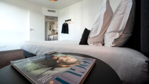 A hotel room with a bed, a magazine on a table, and a view of the kitchen and hallway. -  Nemea Appart Hotel Europe Velizy Villacoublay (Velizy-Villacoublay)