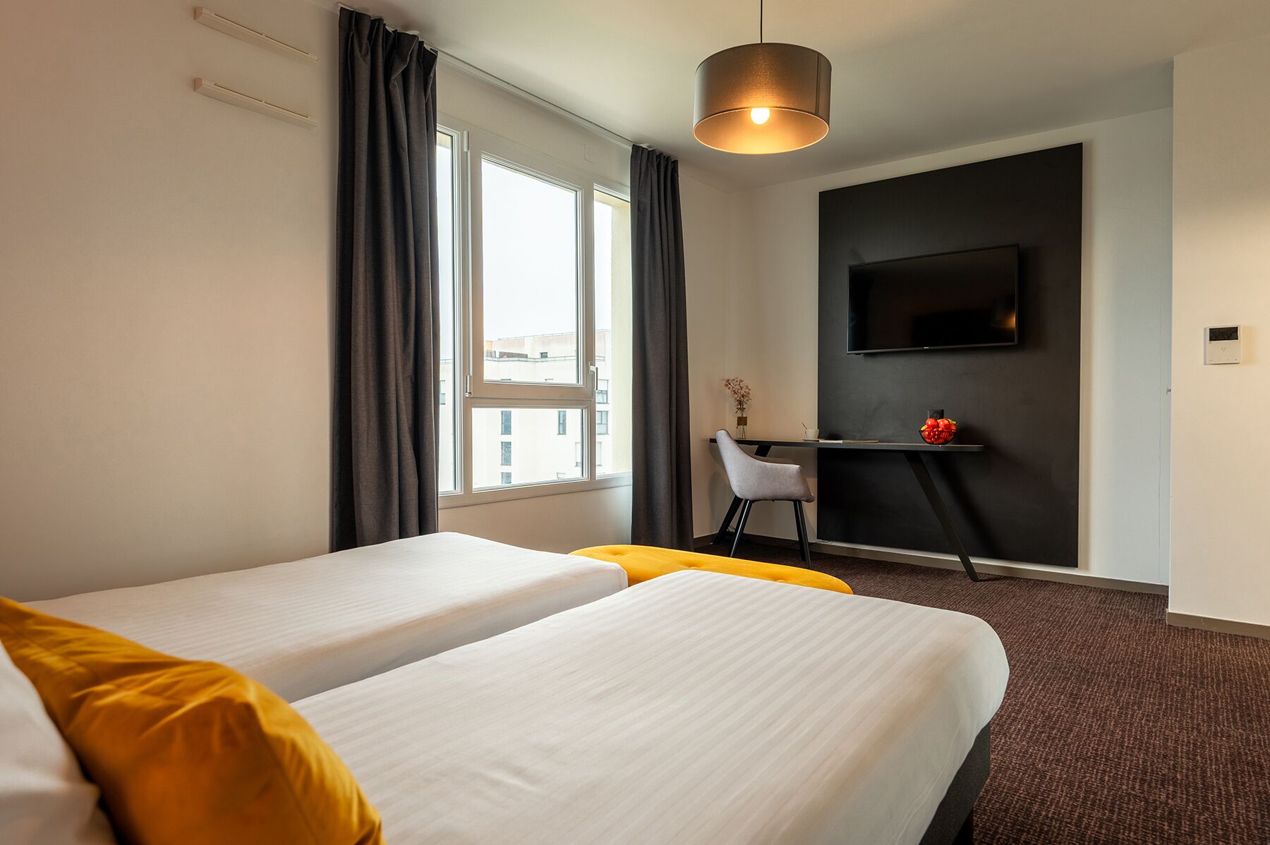 Een hotelkamer met twee bedden, een bureau met stoel, een televisie en een raam met gordijnen.