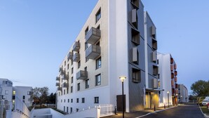 A modern multi-story building with balconies, a gated entrance, and a well-lit pathway. -  Nemea Appart Hotel Europe Velizy Villacoublay (Velizy-Villacoublay)