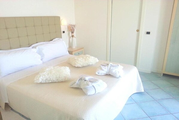 A neatly made bed with pillows and folded towels on a light-colored bedspread. - Ca Bianca (Riccione)