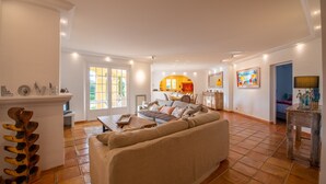 Un salon spacieux avec un grand canapé beige, une table basse en bois et un coin repas à l’arrière-plan.