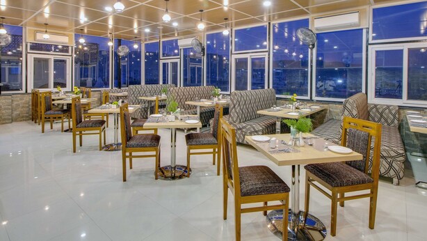 A spacious restaurant with high ceilings, large windows, and a variety of seating options including tables, chairs, and sofas. - Jasoda Heritage Hotel Near Hawa Mahal (Jaipur)