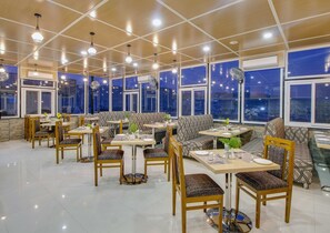 A spacious restaurant with high ceilings, large windows, and a variety of seating options including tables, chairs, and sofas. - Jasoda Heritage Hotel Near Hawa Mahal (Jaipur)