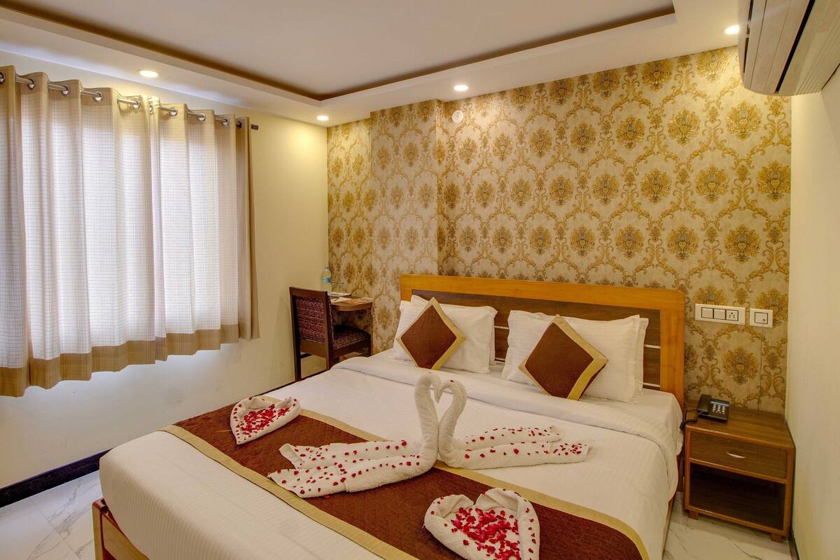 Quarto de hotel com uma cama bem arrumada, mesa de cabeceira com abajur e ar condicionado fixado na parede.
