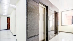 A modern elevator with a metallic finish, adjacent to a hallway with marble flooring and a glass door. - Jasoda Heritage Hotel Near Hawa Mahal (Jaipur)