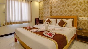 A hotel room with a large bed, a wooden headboard, a bedside table with a phone, and a patterned wallpaper. - Jasoda Heritage Hotel Near Hawa Mahal (Jaipur)