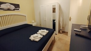 Et hotelværelse med en seng, et natbord, et spejl og en dør, der fører til et andet rum.