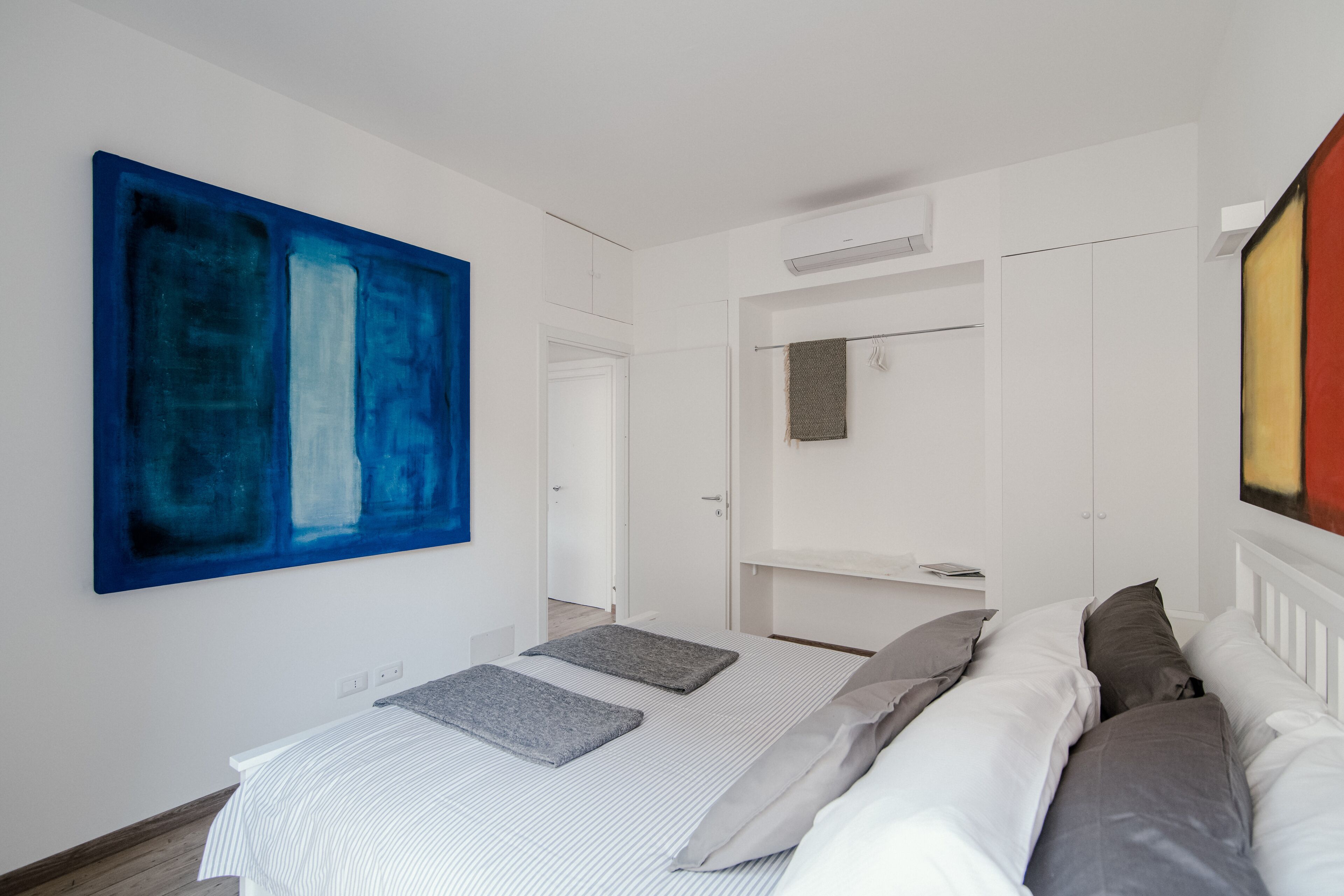 Un dormitorio moderno con un cuadro abstracto grande, una cama bien hecha y un diseño minimalista.