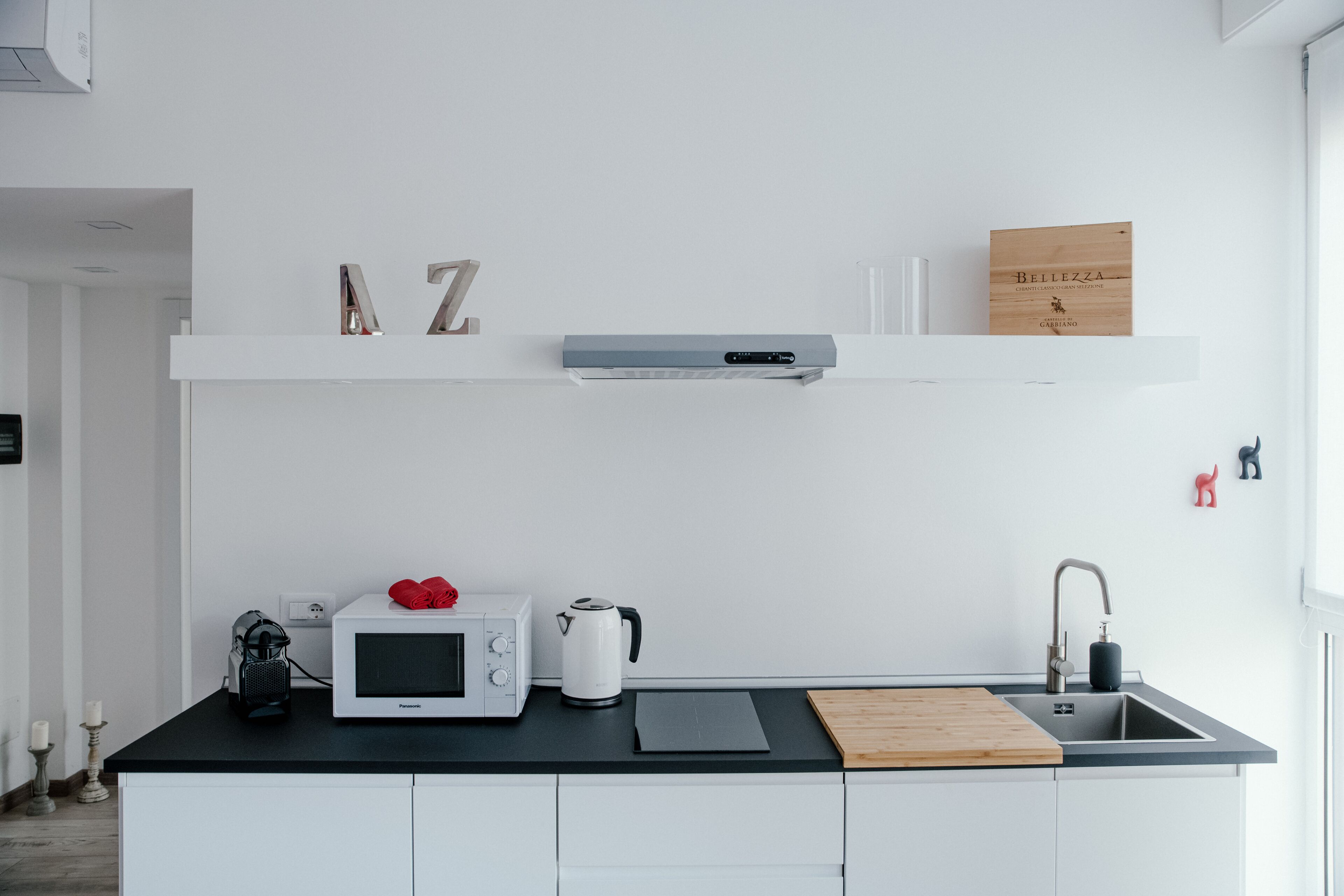 Una cocina moderna con encimera negra, armarios blancos, microondas, hervidor y tabla de cortar de madera.