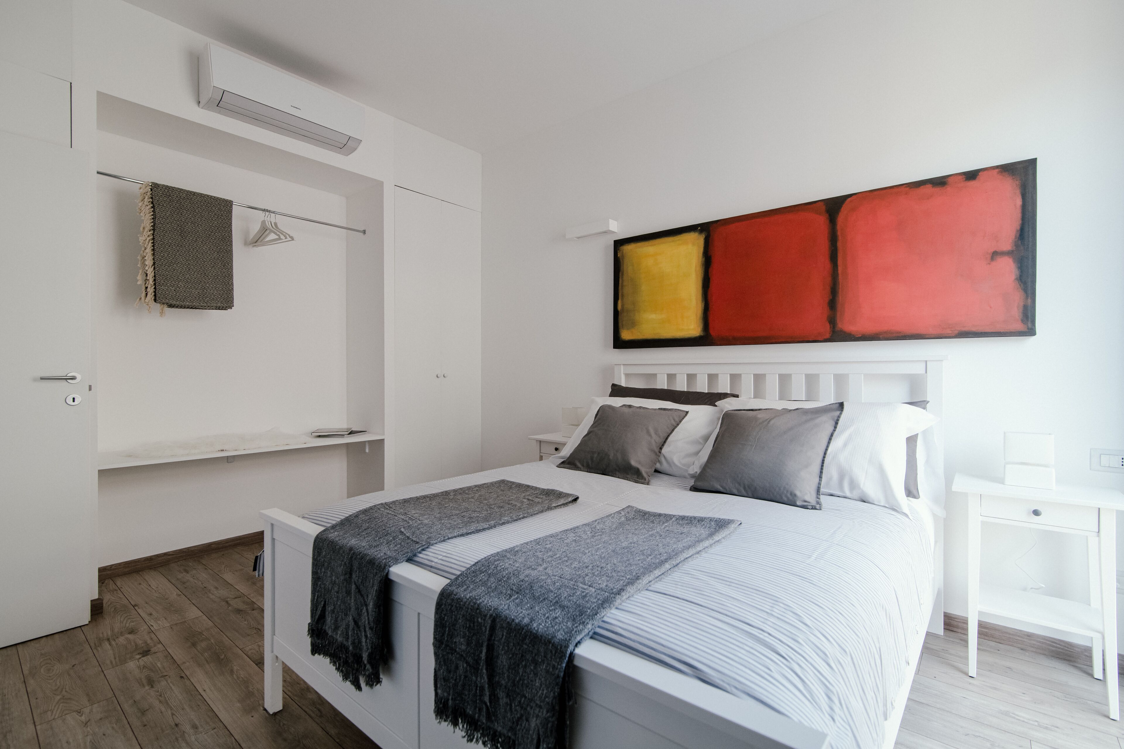 A modern bedroom with a bed, bedside tables, a wardrobe, and a large abstract painting on the wall.
