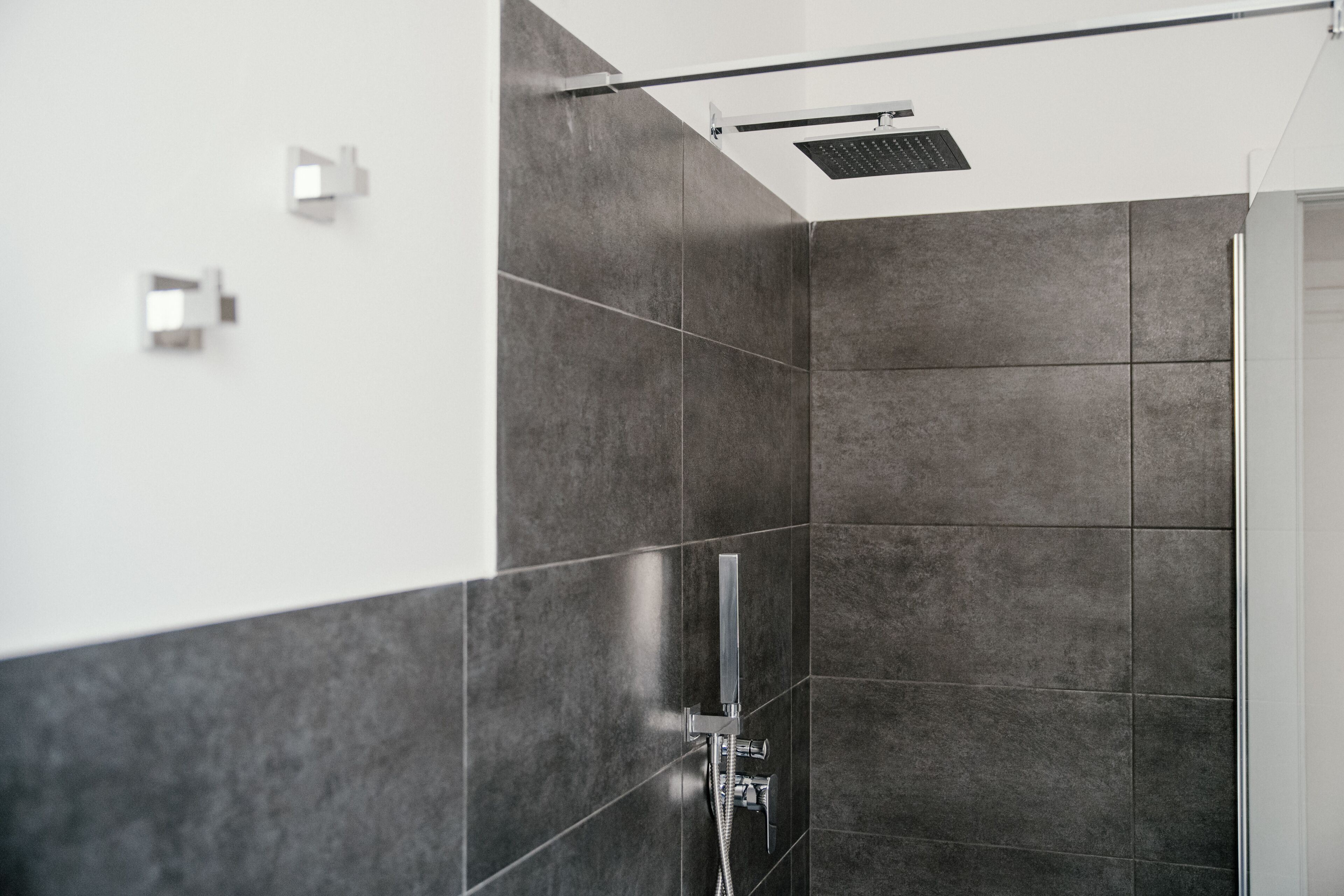 Une salle de bain moderne avec des carreaux de couleur sombre, une pomme de douche et un sèche-mains.