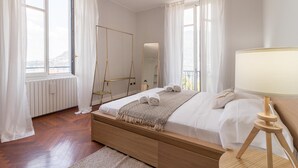 A bedroom with a wooden bed, white bedding, a standing mirror, and a bedside lamp. - Como Lake Vista by My Home in Como (Blevio)