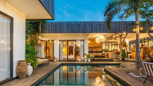 A modern outdoor pool area with a wooden deck, a glass-bottomed pool, and a dining area with outdoor seating. - Fabulous 3BR Boho-chic Style, Umalas With Staff (Kerobokan)