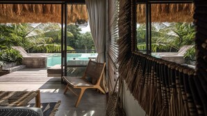 Un espacio habitable moderno y de concepto abierto con un amplio ventanal que da a una piscina y abundante vegetación.