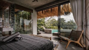 A modern bedroom with a large bed, a wooden chair, a glass shower, and a view of the outdoors. - Batukaru Private Pool Suite 3 (Canggu)