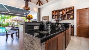 A modern kitchen with a granite countertop, coffee maker, and blender. There is a dining area with a table and chairs, and a thatched umbrella.