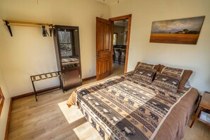 Quarto com cama grande, porta de madeira, porta-roupas e um quadro na parede.
