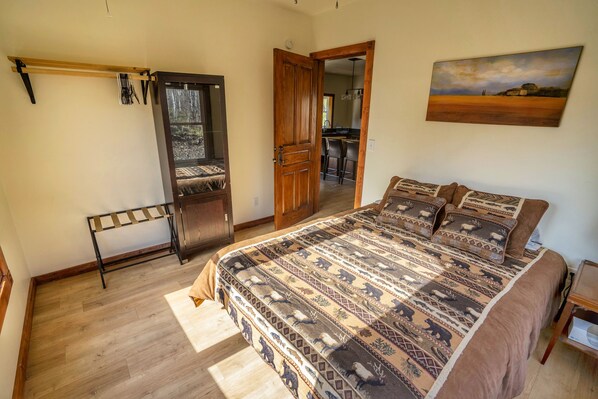 A bedroom with a large bed, a wooden door, a coat rack, and a painting on the wall. - Your Adventure Basecamp In Marble, CO (Marble)