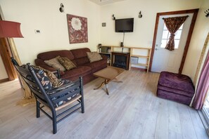 Uma sala de estar com sofá, poltrona, mesa de centro, televisão e lareira.