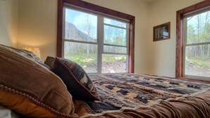 Ein Schlafzimmer mit einem großen Bett, zwei Fenstern und Blick auf einen Wald.