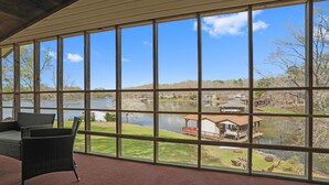 A room with large windows overlooking a lake, featuring a wicker chair and a view of a dock and boats. - Lakefront 4bd-2ba; Deep water; Large Porch; Sleeps 14; Pet friendly (Macon)