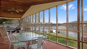 A covered patio with a glass table and chairs, overlooking a lake with boats and a dock. - Lakefront 4bd-2ba; Deep water; Large Porch; Sleeps 14; Pet friendly (Macon)