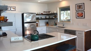 A modern kitchen with a double-door refrigerator, a kettle on the countertop, and a sign indicating the kitchen is open.