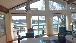 A room with a table and chairs, large windows with a view of a body of water, and a ceiling fan.