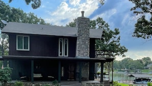 A two-story house with a stone chimney, a porch, and a view of a lake.