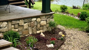 A covered outdoor area with a stone wall, wooden deck, and a view of a lake.
