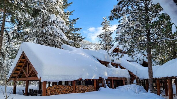 A wooden cabin with a snow-covered roof, surrounded by tall pine trees. - Birch Room 10 - loft room at The Inn At Mazama (Mazama)